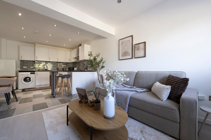 Open-plan living and kitchen area with gray sofa, wooden coffee table, and modern kitchen appliances