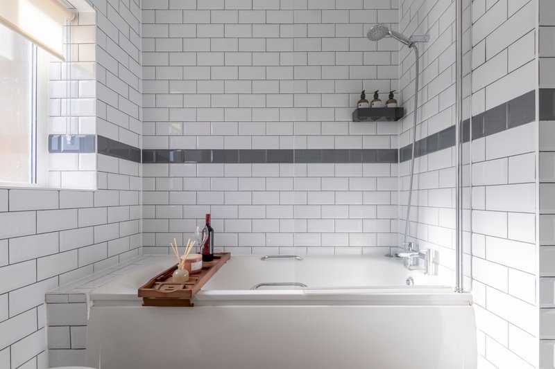 Modern bathroom with white subway tile walls, soaking tub, wooden bath caddy, and overhead shower