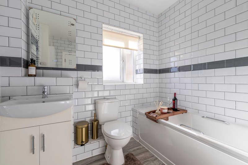 Modern bathroom with white subway tiles, curved sink, toilet, and bathtub with toiletries