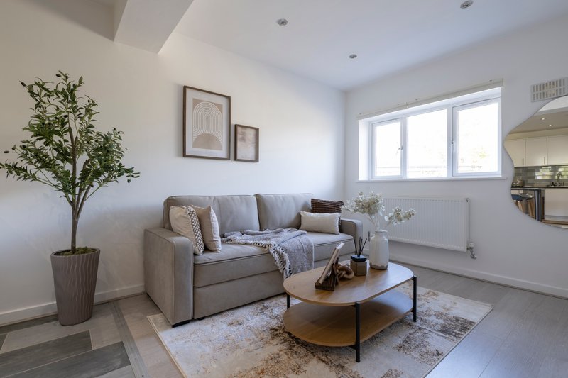 Bright living room with grey upholstered sofa, wooden coffee table, potted plant and framed wall art