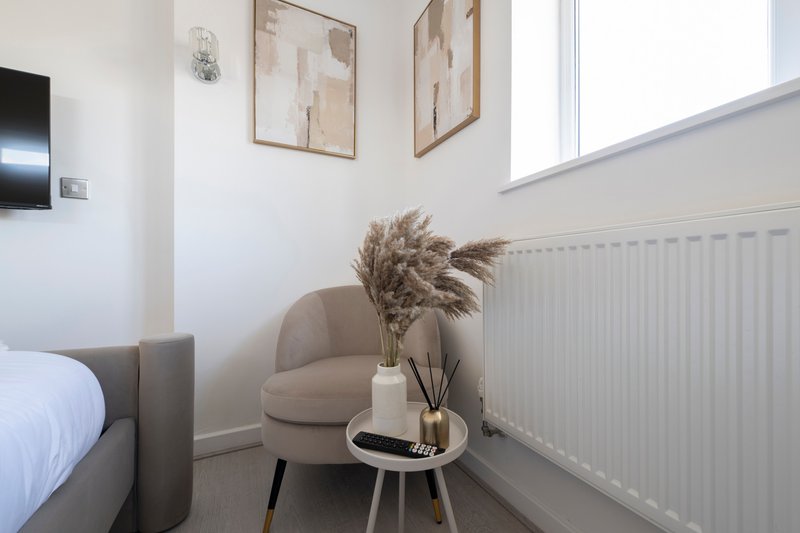 Modern bedroom corner with upholstered chair, small side table with dried flowers, and framed wall art