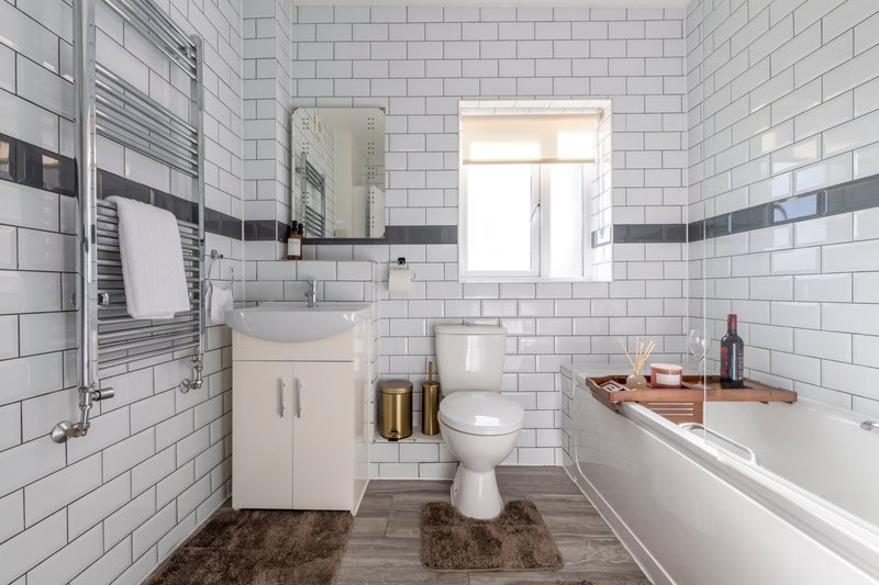Modern bathroom with white subway tiles, vanity sink, toilet, bathtub, and heated towel rail