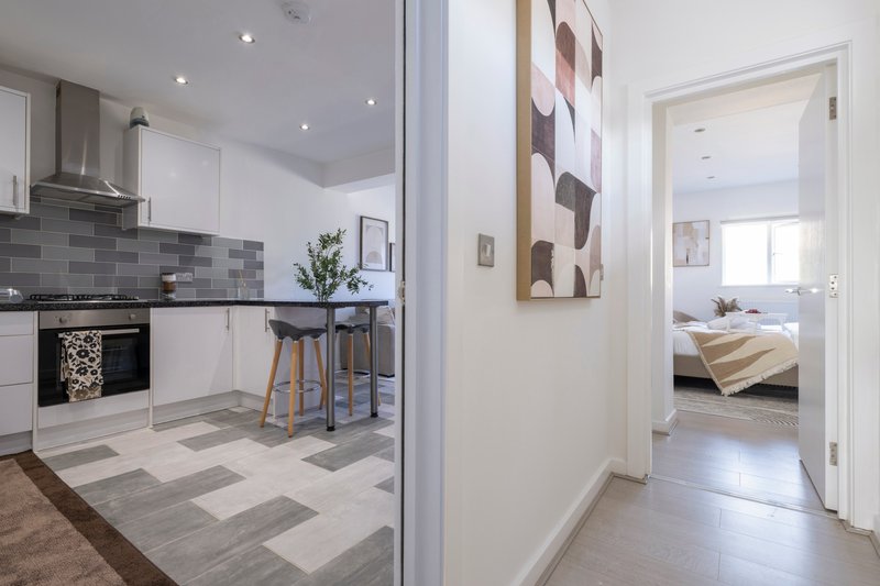 Modern kitchen with white cabinetry, grey tile backsplash, and view through to bedroom