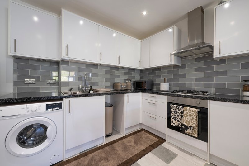 Modern kitchen with white cabinetry, grey tile backsplash, integrated appliances and washing machine