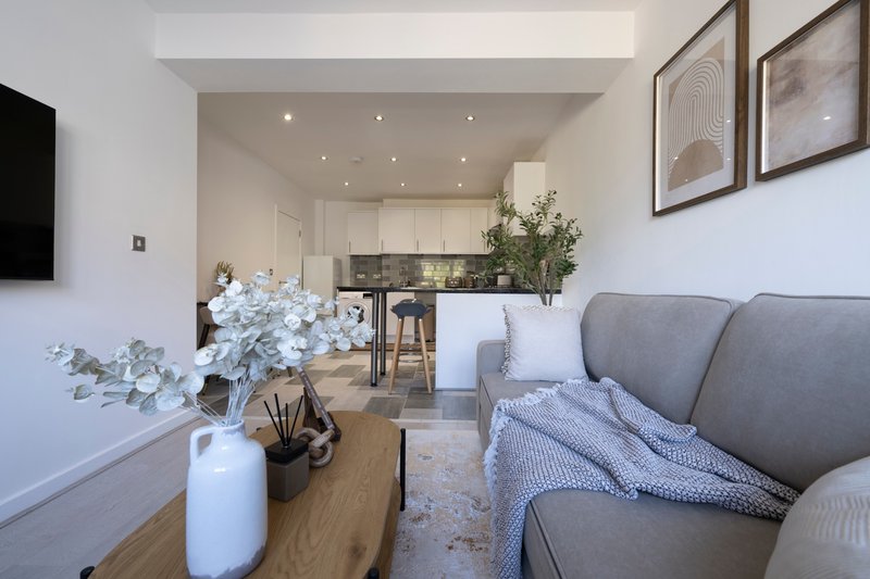Open-plan living room with grey sofa, wooden floor, kitchen area and framed wall art