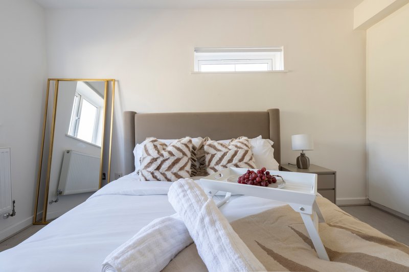 Bright bedroom with grey upholstered bed, white bedding, decorative pillows and standing mirror