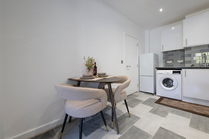 Modern kitchen with dining table, two chairs, washing machine and white cabinetry