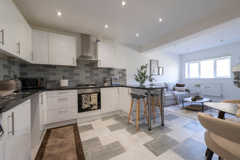 Open-plan kitchen and living area with white cabinetry, gray tile backsplash, breakfast bar seating, and comfortable lounge furniture