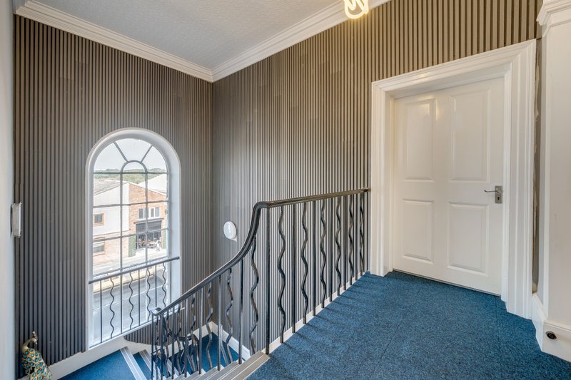 Landing with arched window, metal staircase railing, blue carpet and white door