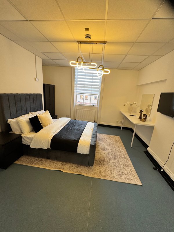 Modern bedroom with black upholstered bed, cream bedding, desk, pendant light and window