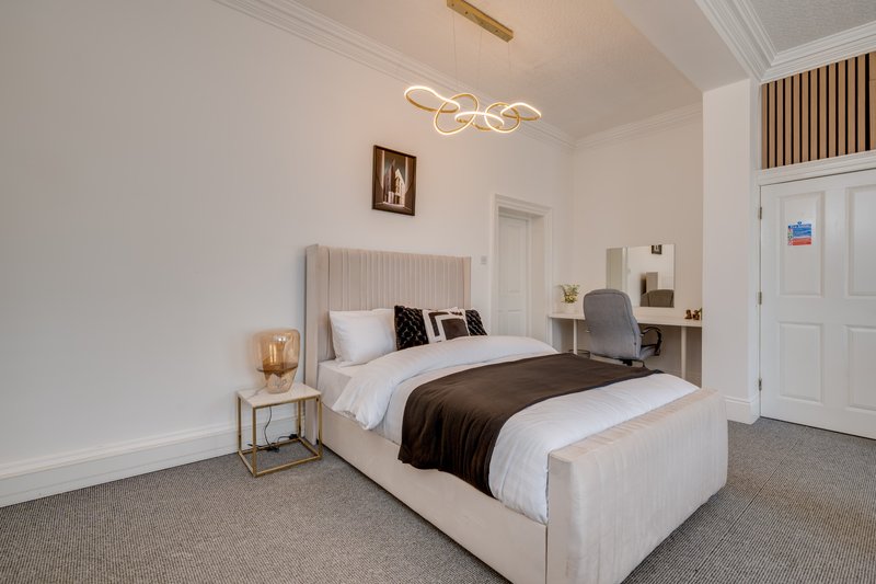 Modern bedroom with cream upholstered bed, brown throw, pendant ceiling light and en-suite door