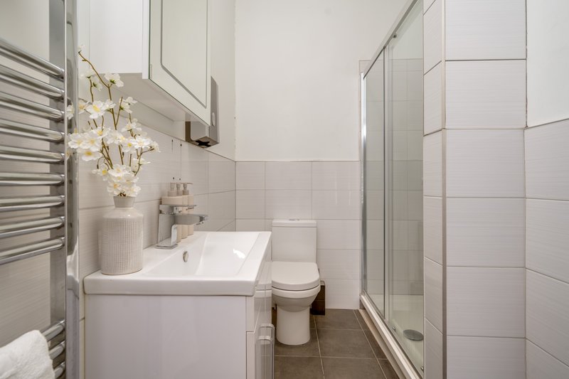 Modern bathroom with white basin, toilet, towel rail, shower enclosure and decorative plants