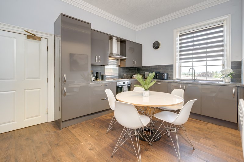 Modern kitchen with grey cabinetry, white dining table, wooden flooring and striped window blinds