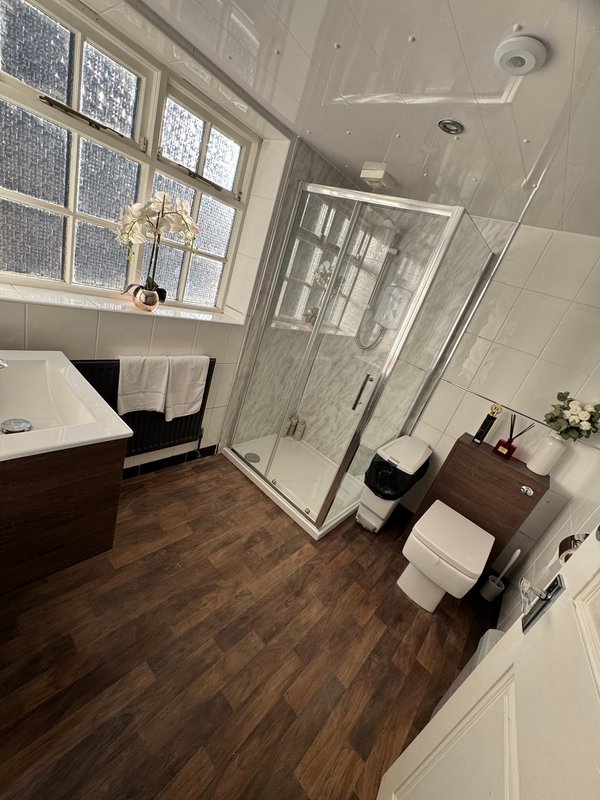 Modern bathroom with wooden flooring, bathtub, enclosed shower, toilet and vanity