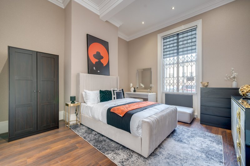 Spacious bedroom with double bed, dark wardrobe, orange abstract artwork, and bright window