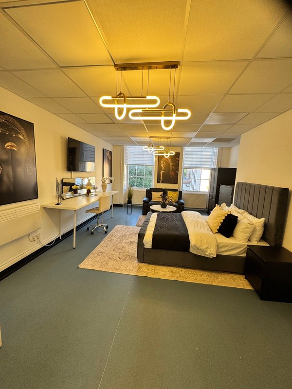 Modern bedroom with black bed, yellow accents, neon light fixture and desk area