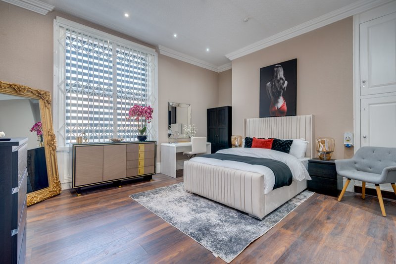 Luxury bedroom with upholstered bed, wooden floor, modern furnishings and gold-framed mirror