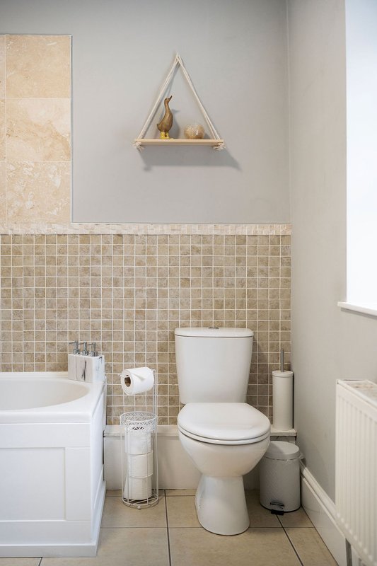 Modern bathroom with toilet, sink, beige tile backsplash and wall-mounted shelf