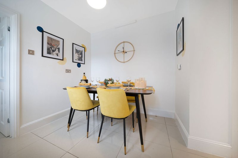 Bright dining area with black table, yellow chairs, framed wall art and round clock