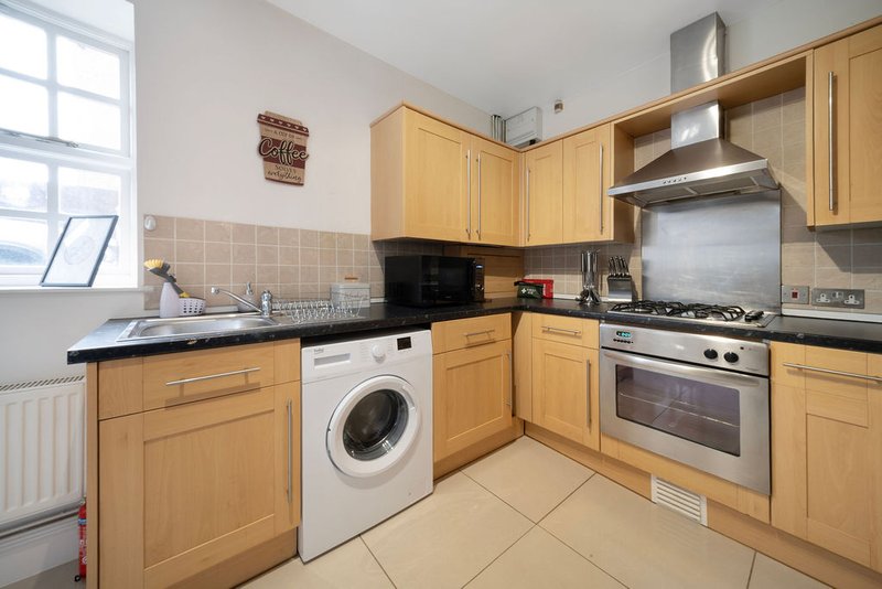 Kitchen with wooden cabinets, stainless steel appliances, washing machine, and tiled floor