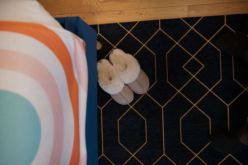 Bedroom floor with pair of beige slippers on black geometric patterned rug