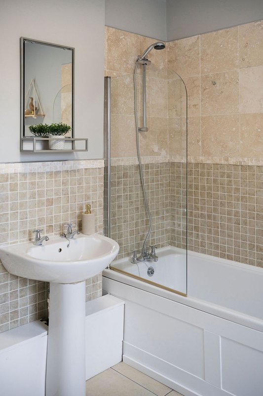 Clean bathroom with pedestal sink, mirror, tiled walls and shower enclosure