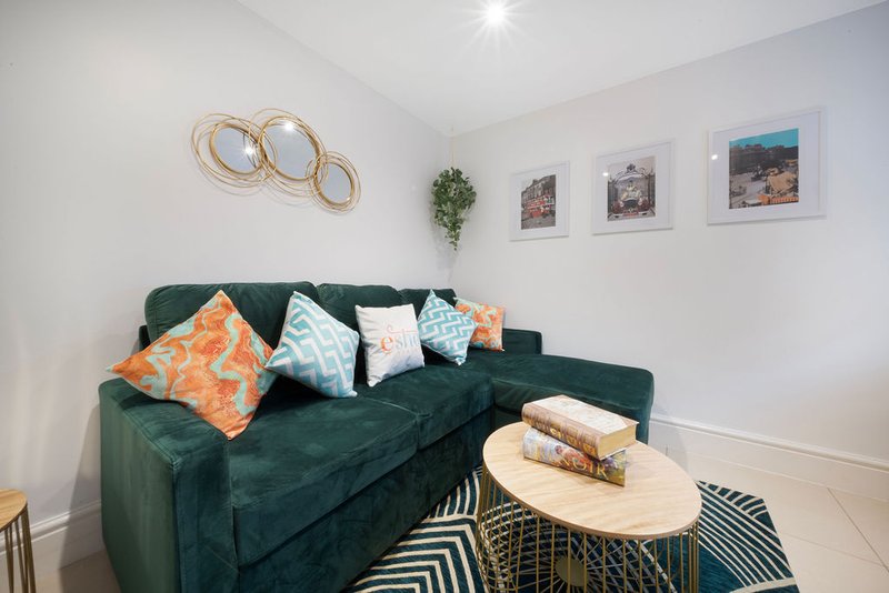 Modern living room with green velvet sofa, colorful cushions, wooden coffee table, and wall art