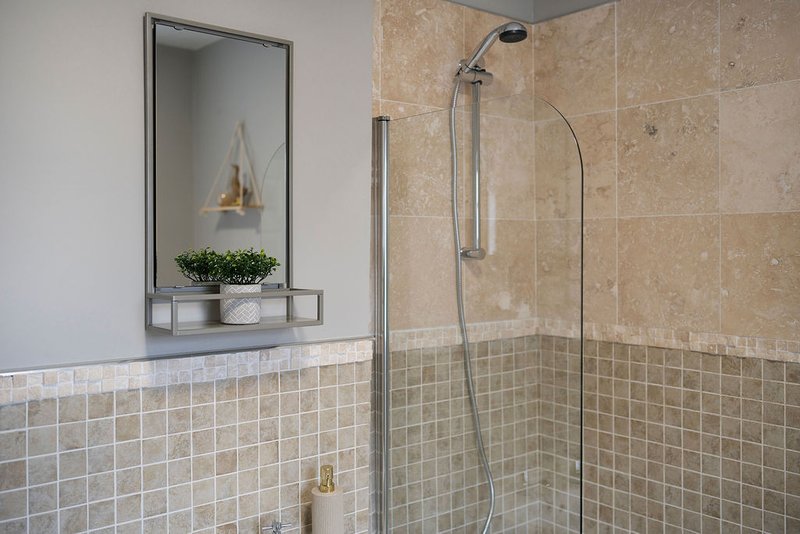 Bathroom with walk-in shower, tiled walls, mirror with shelf, and potted plant
