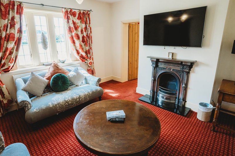 Living room with daybed, fireplace, TV, round wooden table and red patterned carpet