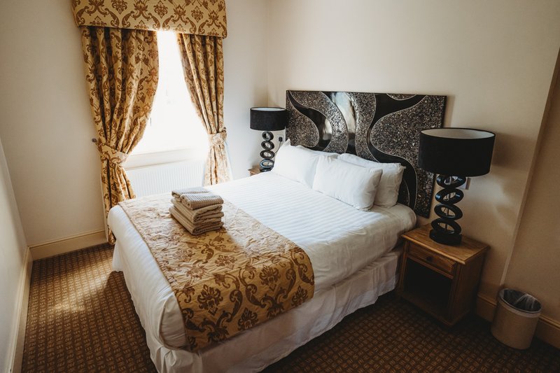 Bedroom with double bed, patterned headboard, gold curtains and bedside table