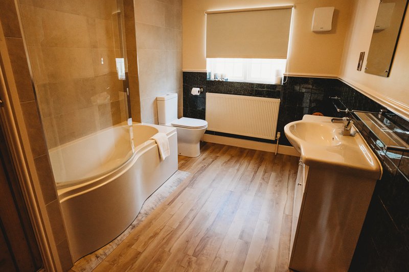 Bathroom with curved bathtub, sink vanity, wooden flooring, and window with blind