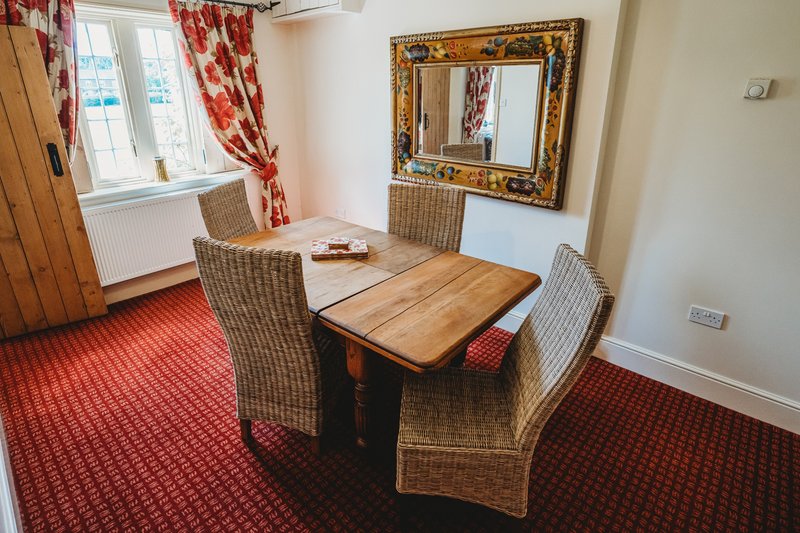 Dining area with wooden table, wicker chairs, red patterned carpet and curtains