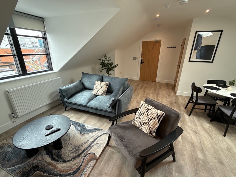 Modern attic living room with blue sofa, black coffee table, dining area and sloped ceiling