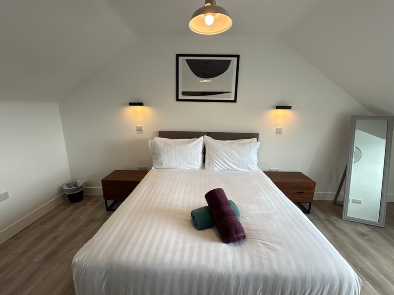 Modern bedroom with white bed, wooden nightstands, pendant light, and framed wall art