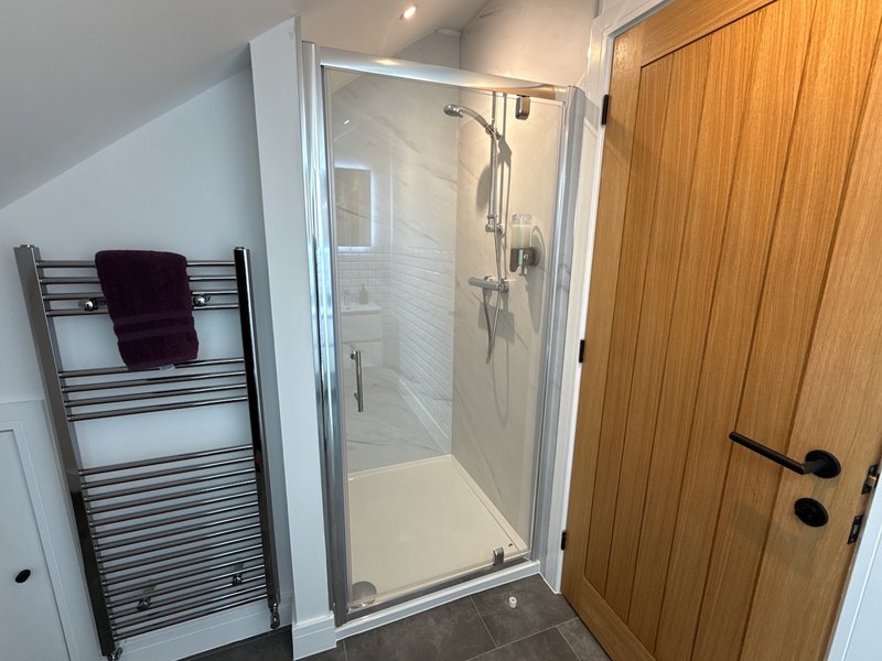 Modern bathroom with walk-in shower, heated towel rail, and wooden door