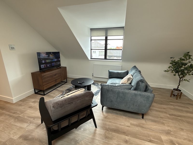 Attic living room with grey sofa, wooden chair, TV dresser and skylight window