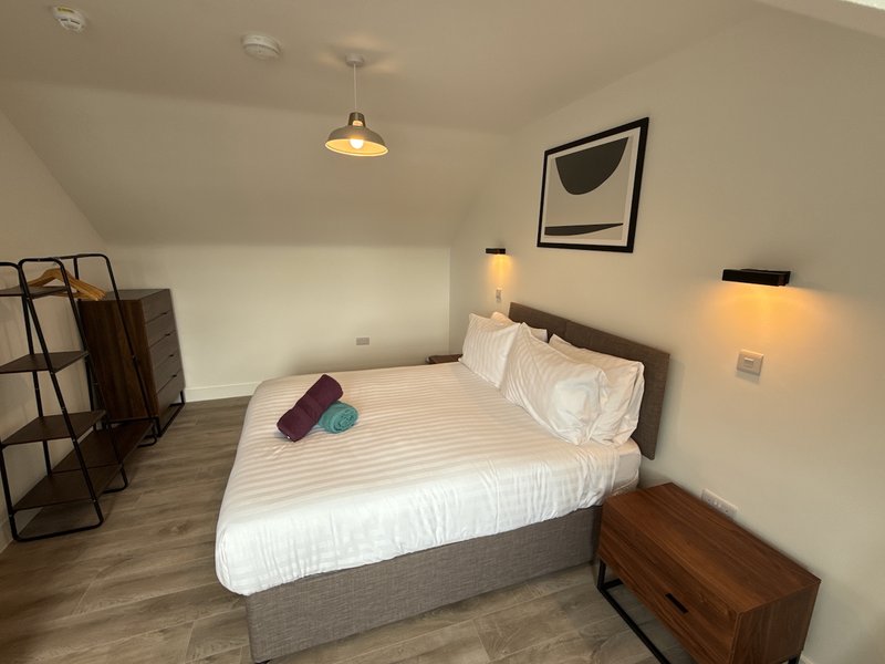 Modern bedroom with double bed, white bedding, wooden floor, pendant light and wall art