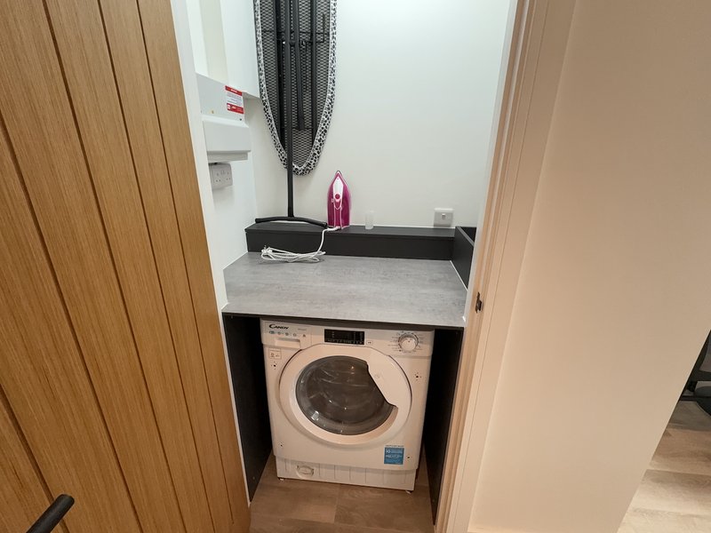 Compact laundry room with front-load washing machine, counter space, and storage shelf