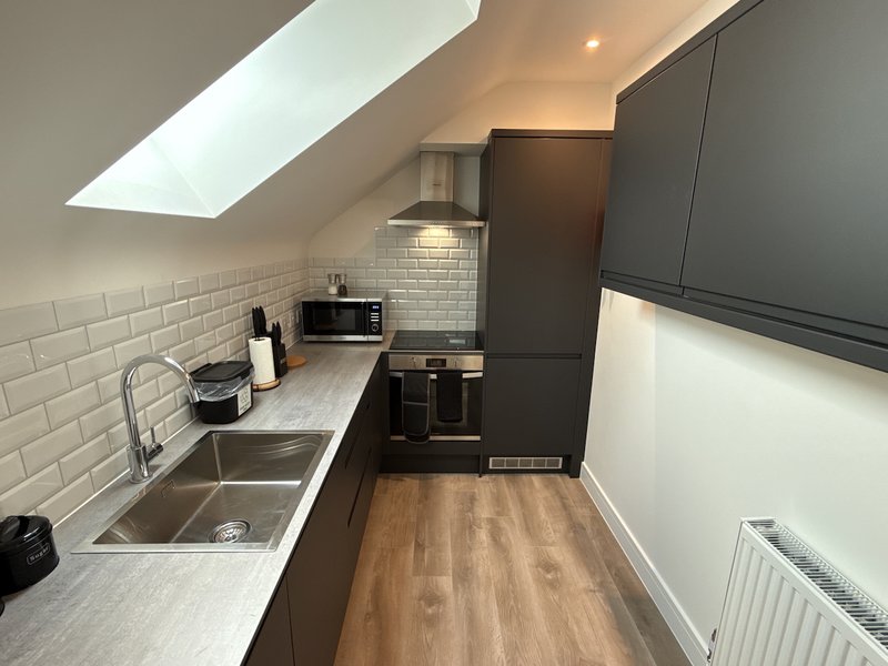Modern galley kitchen with white subway tiles, stainless steel sink, dark cabinetry and wooden flooring