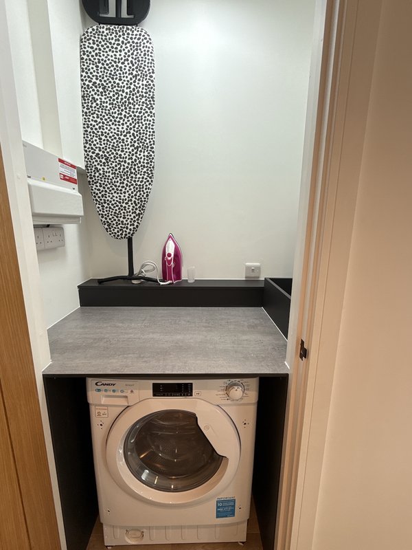 Laundry room with washing machine, ironing board, iron, and storage shelf