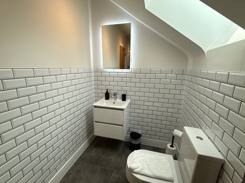 Modern bathroom with white subway tile walls, vanity sink, toilet, and illuminated mirror