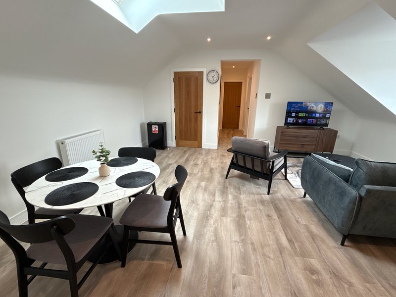 Open-plan attic room with dining table, black chairs, sofa, TV and wooden flooring