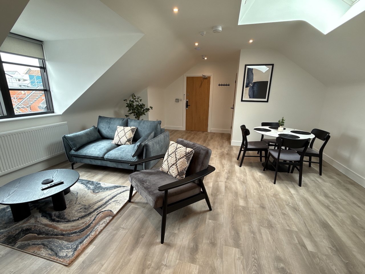 Open-plan living space with blue sofa, brown armchair, dining table and skylight windows