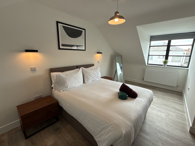 Modern bedroom with double bed, white bedding, wooden nightstand, pendant light and wall art