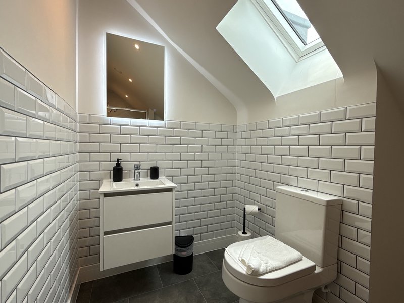 Modern bathroom with white subway tile walls, vanity sink, toilet, mirror and skylight