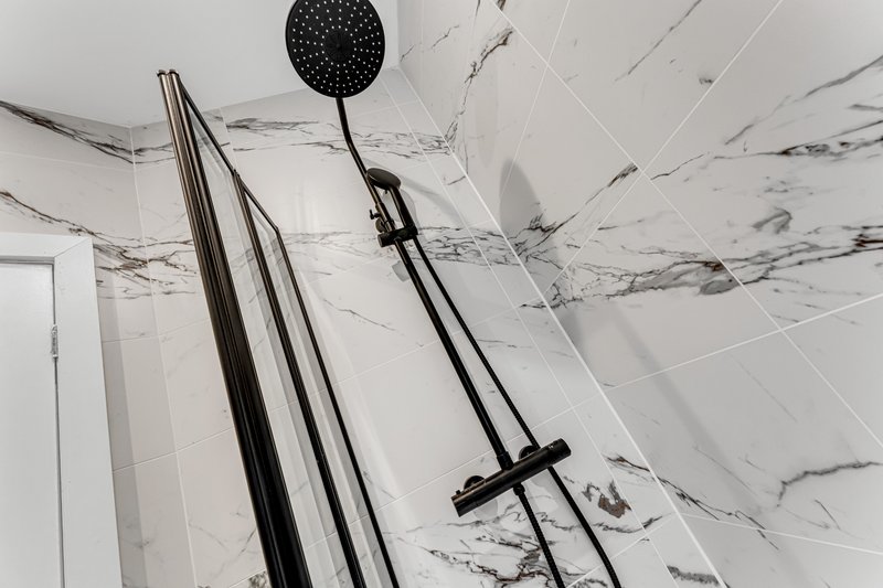 Modern bathroom ceiling with marble effect tiles, black shower head and rail fixtures