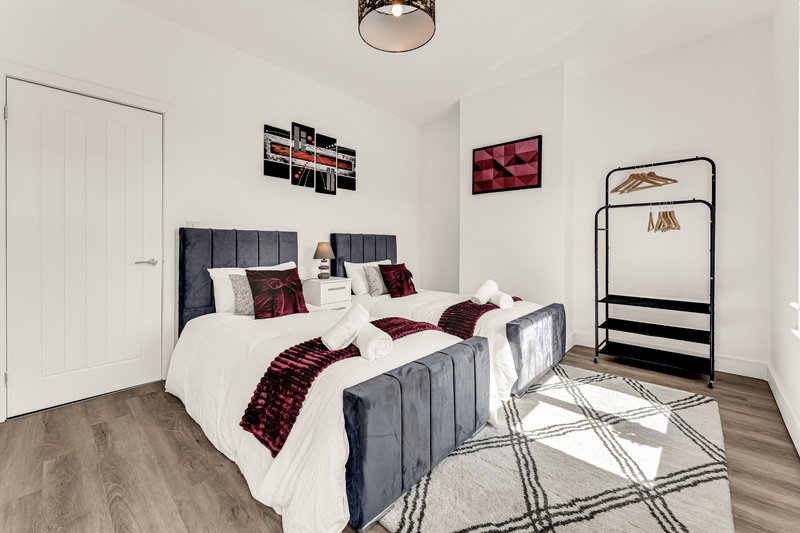 Modern bedroom with grey upholstered bed, white bedding, burgundy accents, and wooden floor