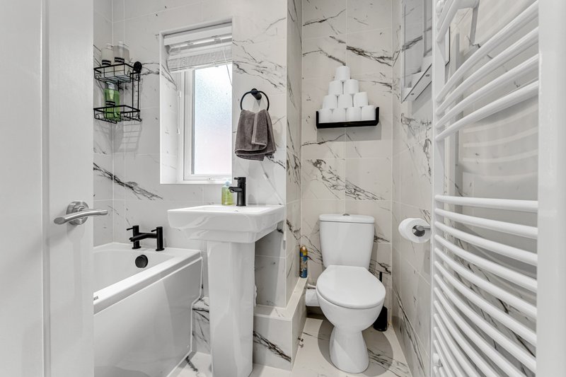 Modern bathroom with pedestal sink, toilet, heated towel rail and marble-effect tiles