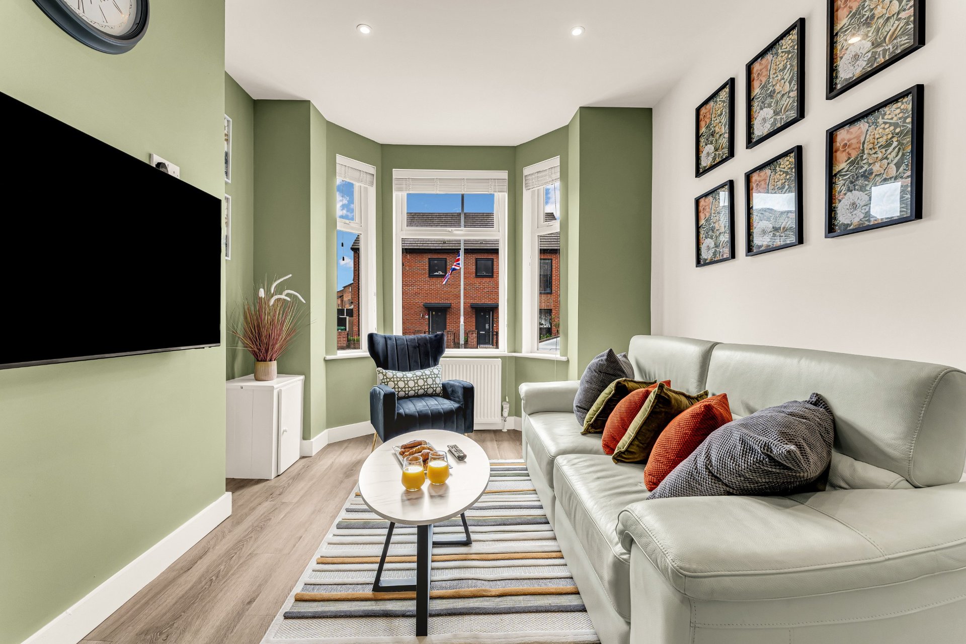 Modern living room with white sofa, wall-mounted TV, bay window, and framed wall art