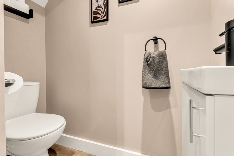 Clean modern WC with white toilet, sink vanity, towel rail and neutral walls
